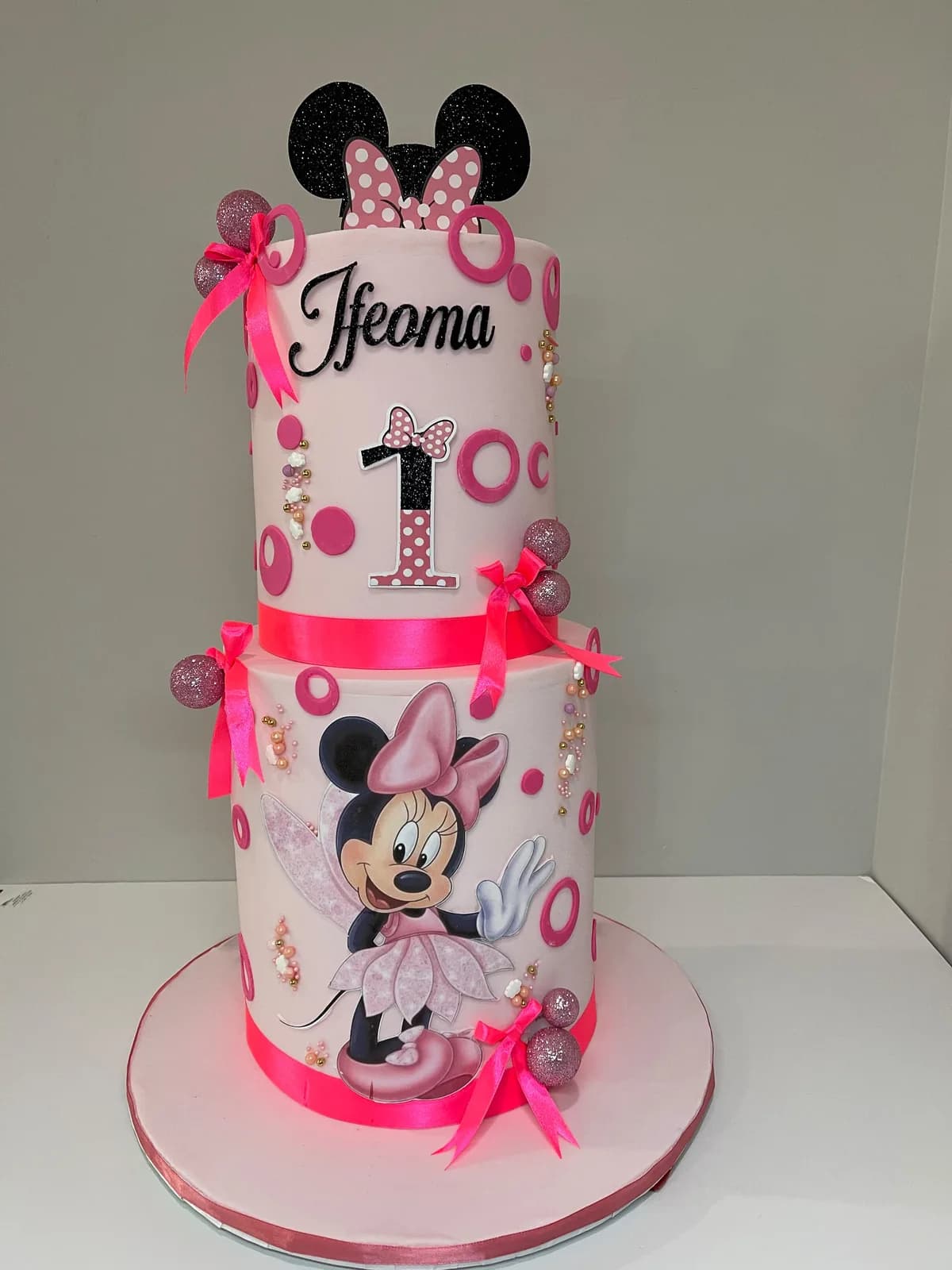 A two-tier pink Minnie Mouse first birthday cake by Cakes by AbimSugar